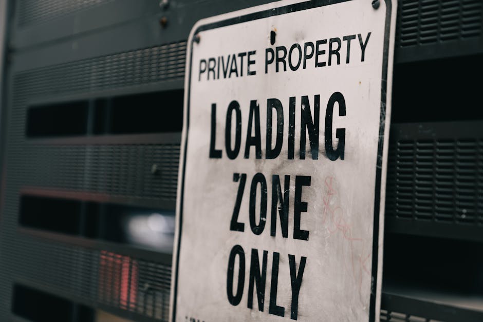 A close-up view of a white metal sign attached to a dark grey or black vented building exterior. The sign displays the text 'PRIVATE PROPERTY LOADING ZONE ONLY' in bold, black capital letters. The bac