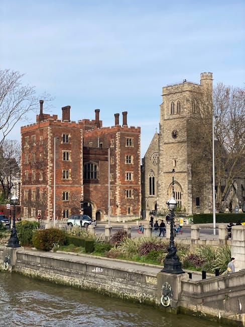 A photograph of historic stone buildings with medieval architectural features, including small rectangular windows and crenellated battlements, captures the exterior of Lambeth Palace near Waterloo St